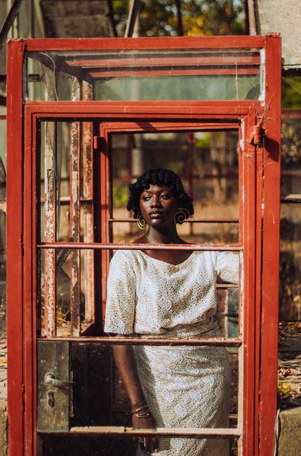 Stylish woman in white lace dress framed by a vintage red doorway outdoors.