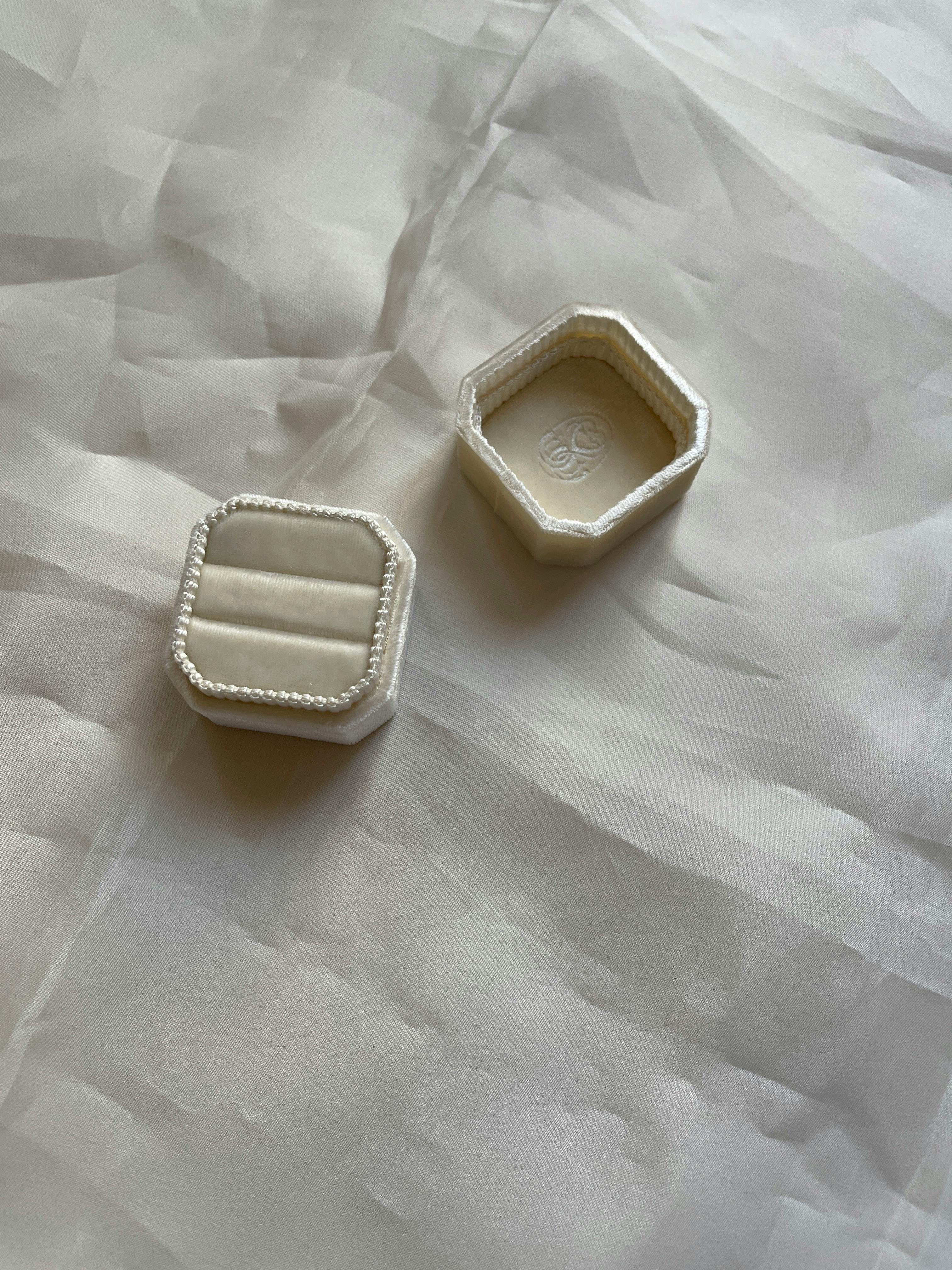 A chic hexagonal ring box on an ivory satin surface, perfect for weddings.