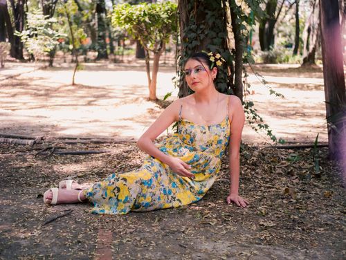 Free A woman in a colorful floral dress sits gracefully in a sunlit park setting, enjoying a peaceful moment. Stock Photo