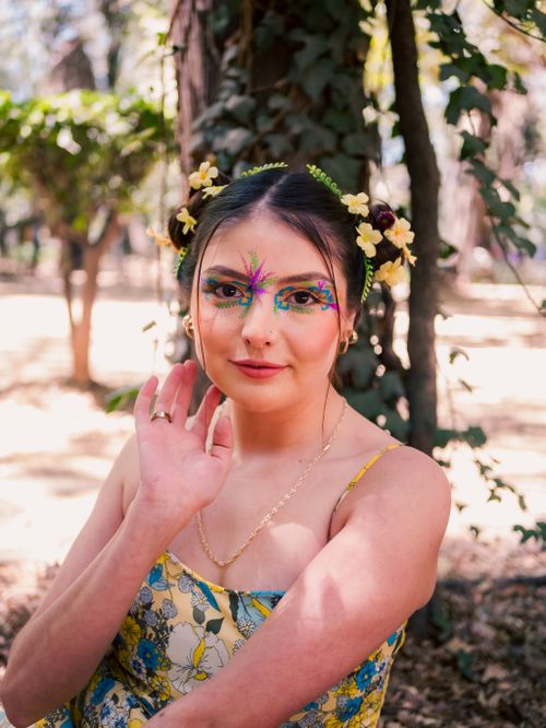 Free Young woman with colorful face paint and floral accessories in a vibrant park setting. Stock Photo