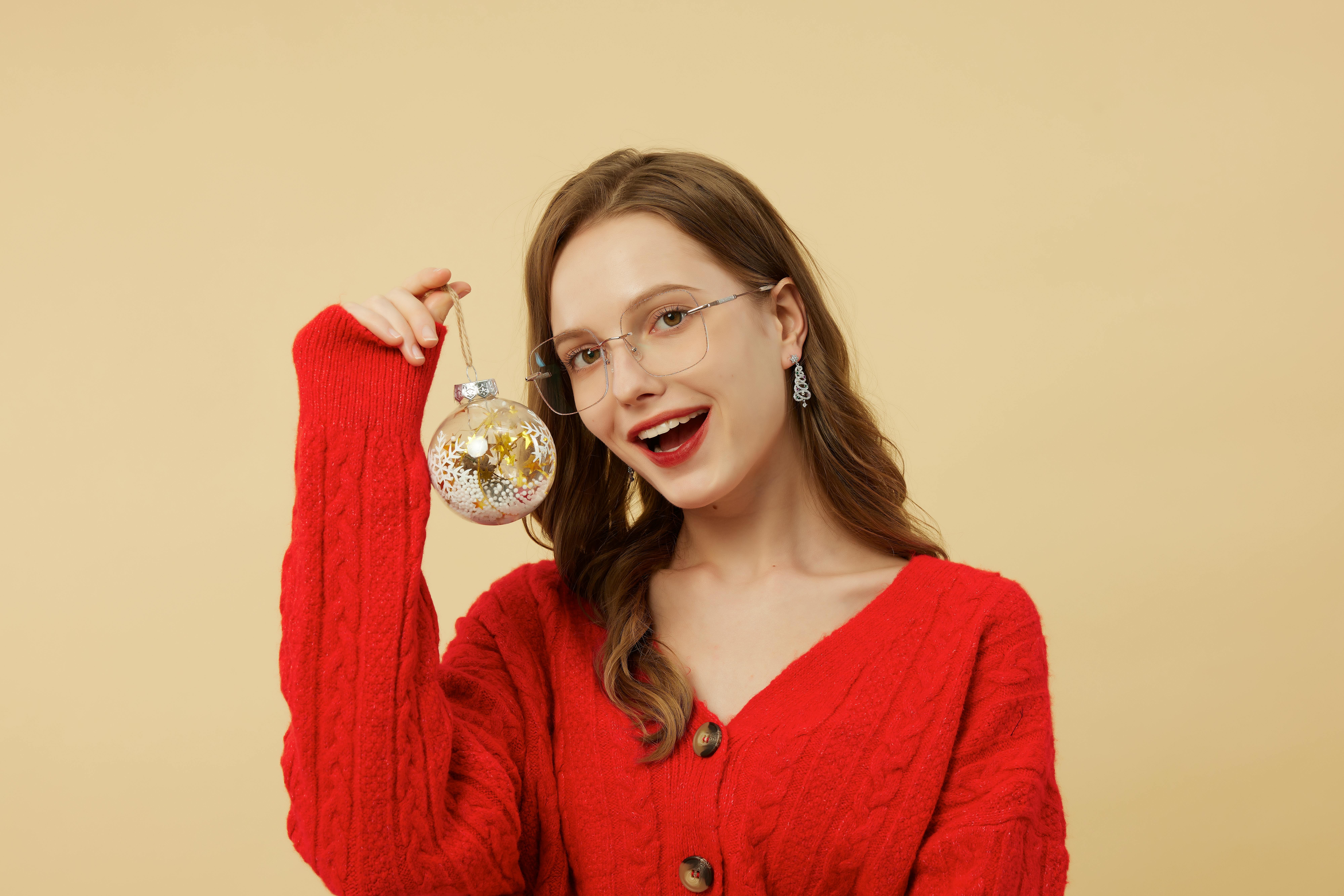 Miễn phí Người phụ nữ mỉm cười mặc áo len đỏ, cầm vật trang trí lễ hội trên nền trung tính. Ảnh lưu trữ