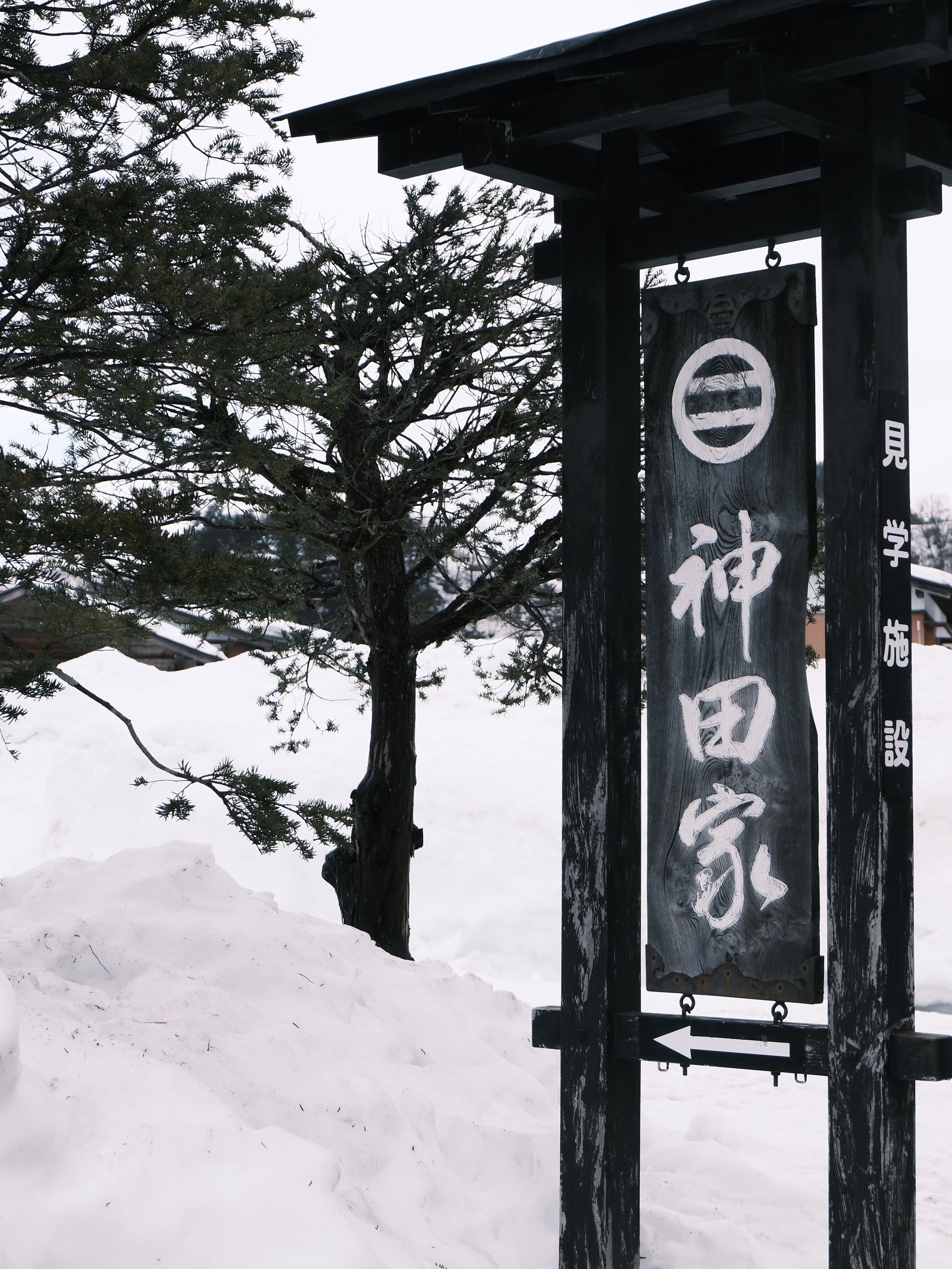 A traditional wooden sign in a snowy landscape in Takayama, Gifu Prefecture, Japan.