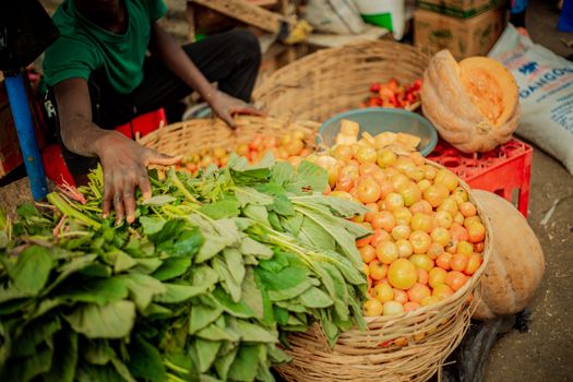 Colorful vegetables and fruits in a bustling market setting. A hand reaches for fresh greens in a basket.