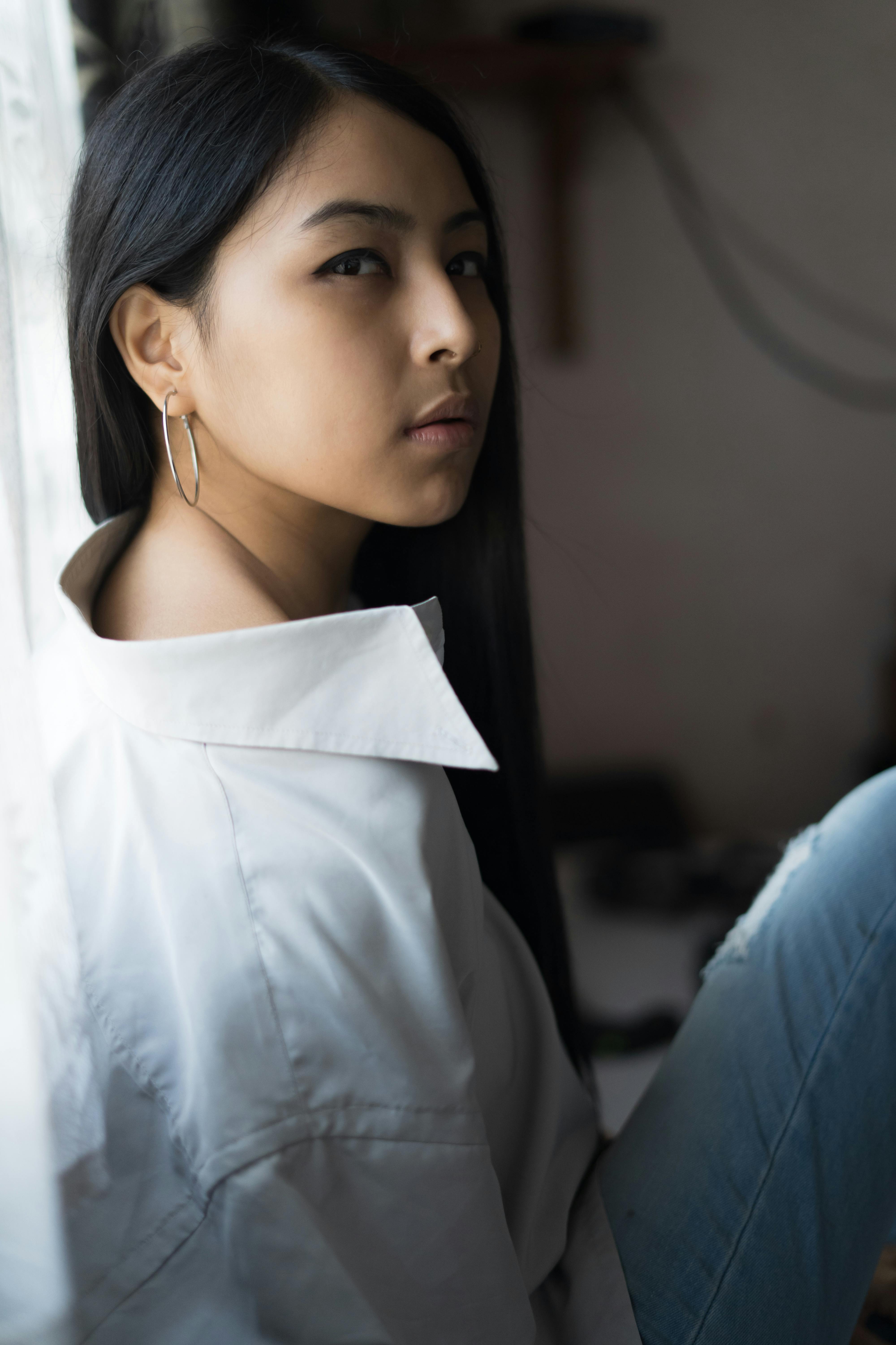 一位穿着白衬衫的优雅年轻女子若有所思地坐在窗前