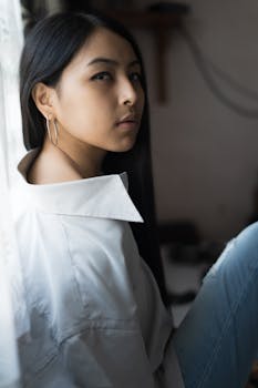 一位穿着白衬衫的优雅年轻女子若有所思地坐在窗前