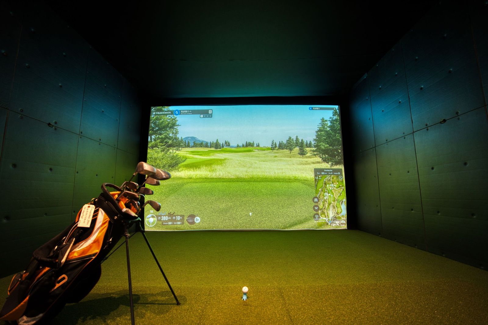 Modern indoor golf simulator with projection screen showing a realistic fairway
