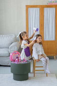 Two girls play hairdresser in a cozy room, using toy styling tools.
