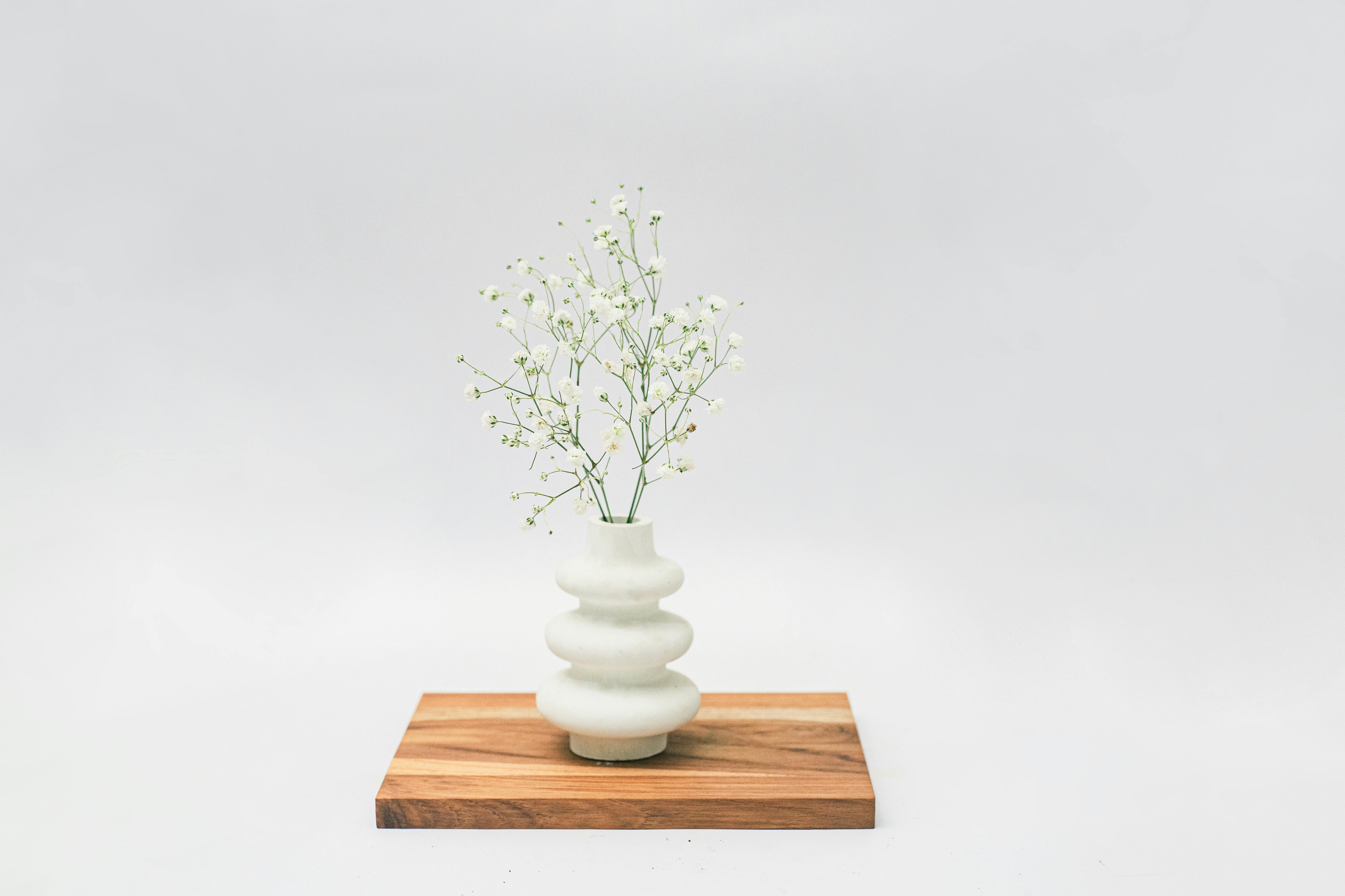 Beautiful baby's breath arrangement in a modern vase on wooden board. Minimalist decor with a soft, serene feel.