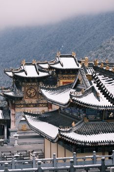 A scenic view of snow-covered rooftops in a traditional Chinese temple amidst mountains.