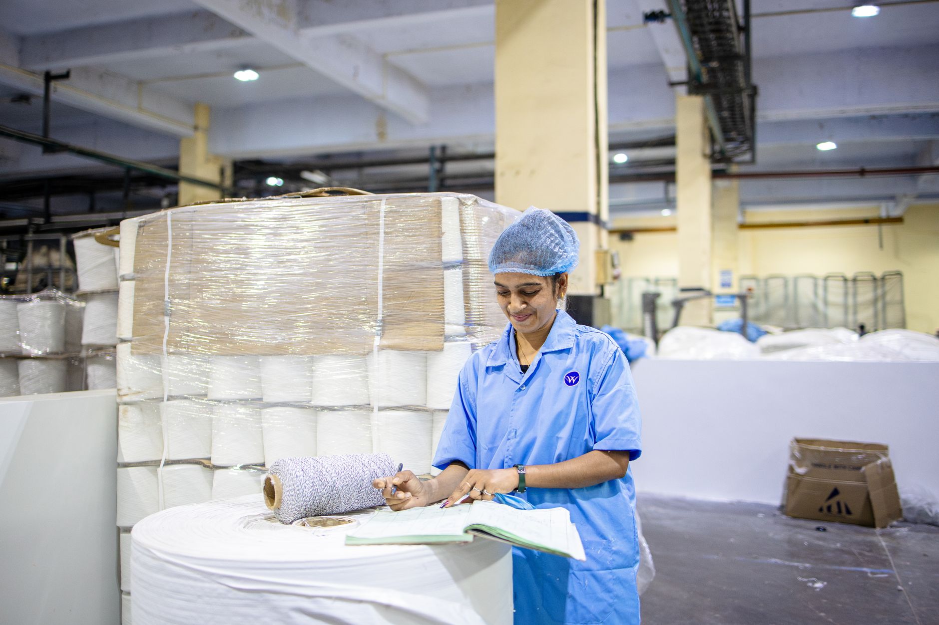 A factory worker records details in a textile manufacturing plant, showcasing industry and precision.