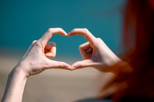 Free Close-up of hands forming a heart shape on a blurred blue background, symbolizing love or friendship. Stock Photo
