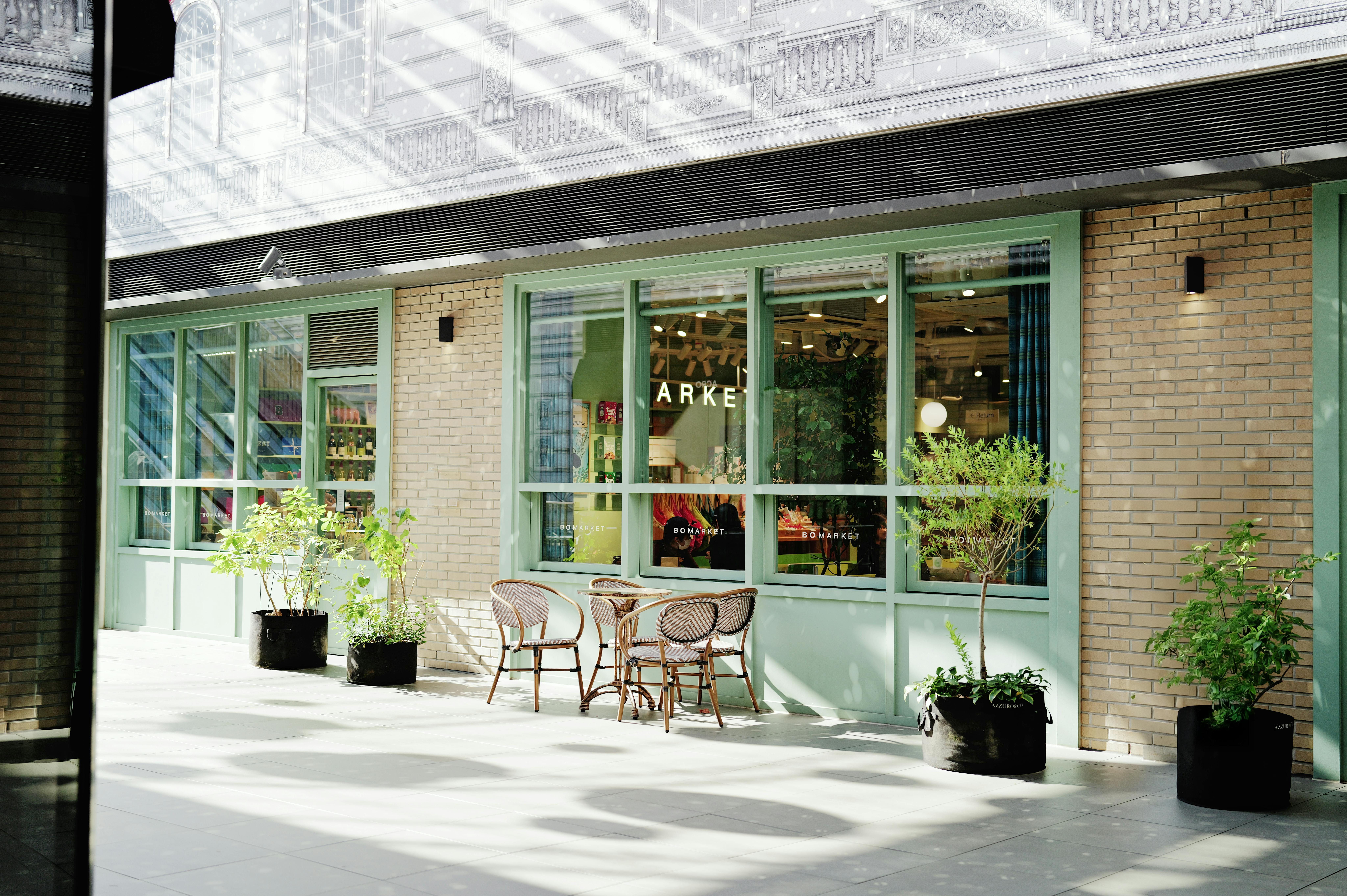 A cozy outdoor cafe setting with wicker chairs and potted plants against a stylish brick and glass facade.