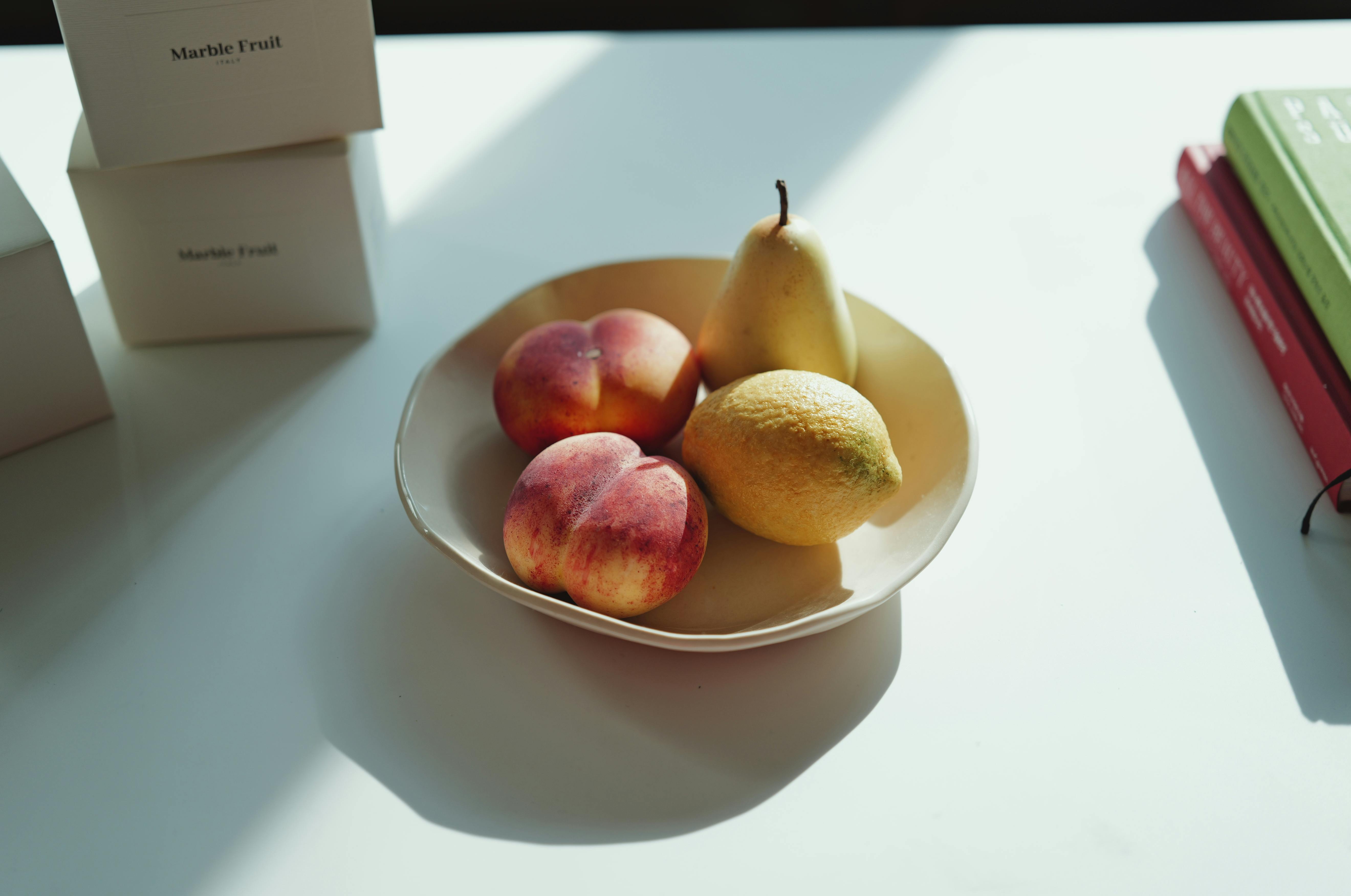 Aesthetic still life of peaches, pear, and lemon on a sunlit table.