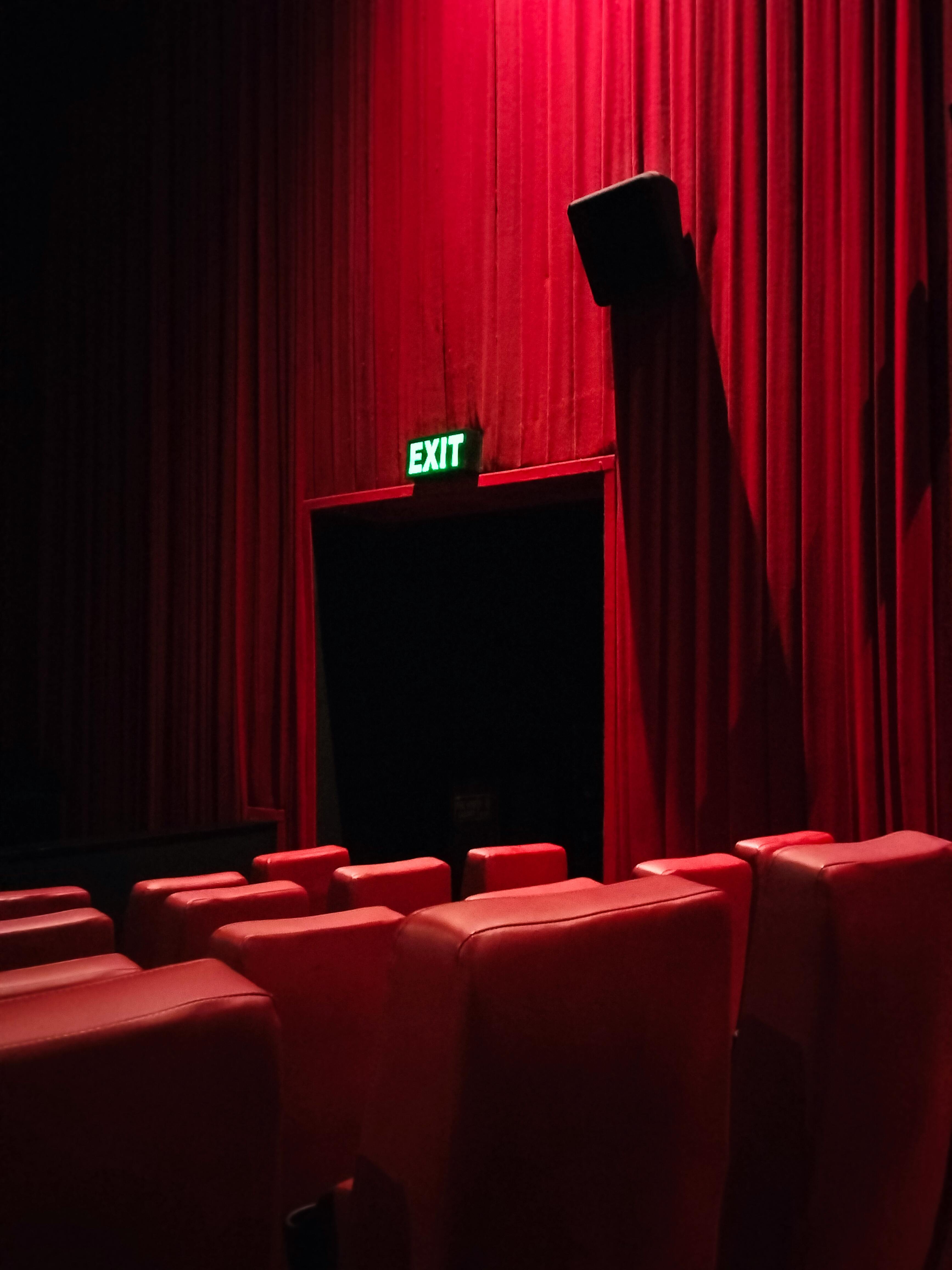 Kostnadsfria Röda teaterstolar och gardiner framhäver en dramatisk utgångsscen från biografen. Stock foto