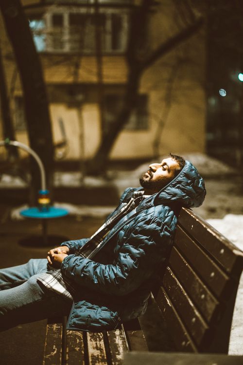 Free A man in a hooded jacket relaxing on a park bench at night in Almaty, Kazakhstan. Stock Photo