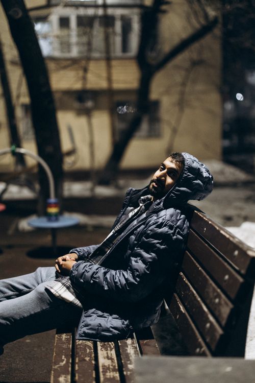 Free A man in winter clothing relaxes on a wooden bench at night in Almaty, Kazakhstan. Stock Photo