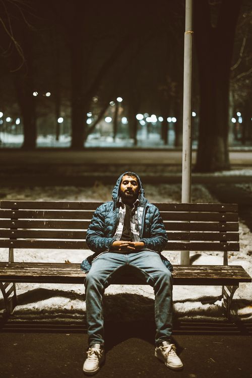 Free A solitary man sits on a bench in a dimly lit snowy park, evoking introspection. Stock Photo