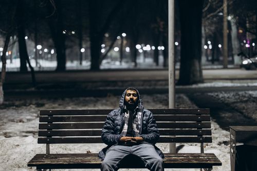 Free A man sits thoughtfully on a bench in snowy Almaty park at night. Stock Photo
