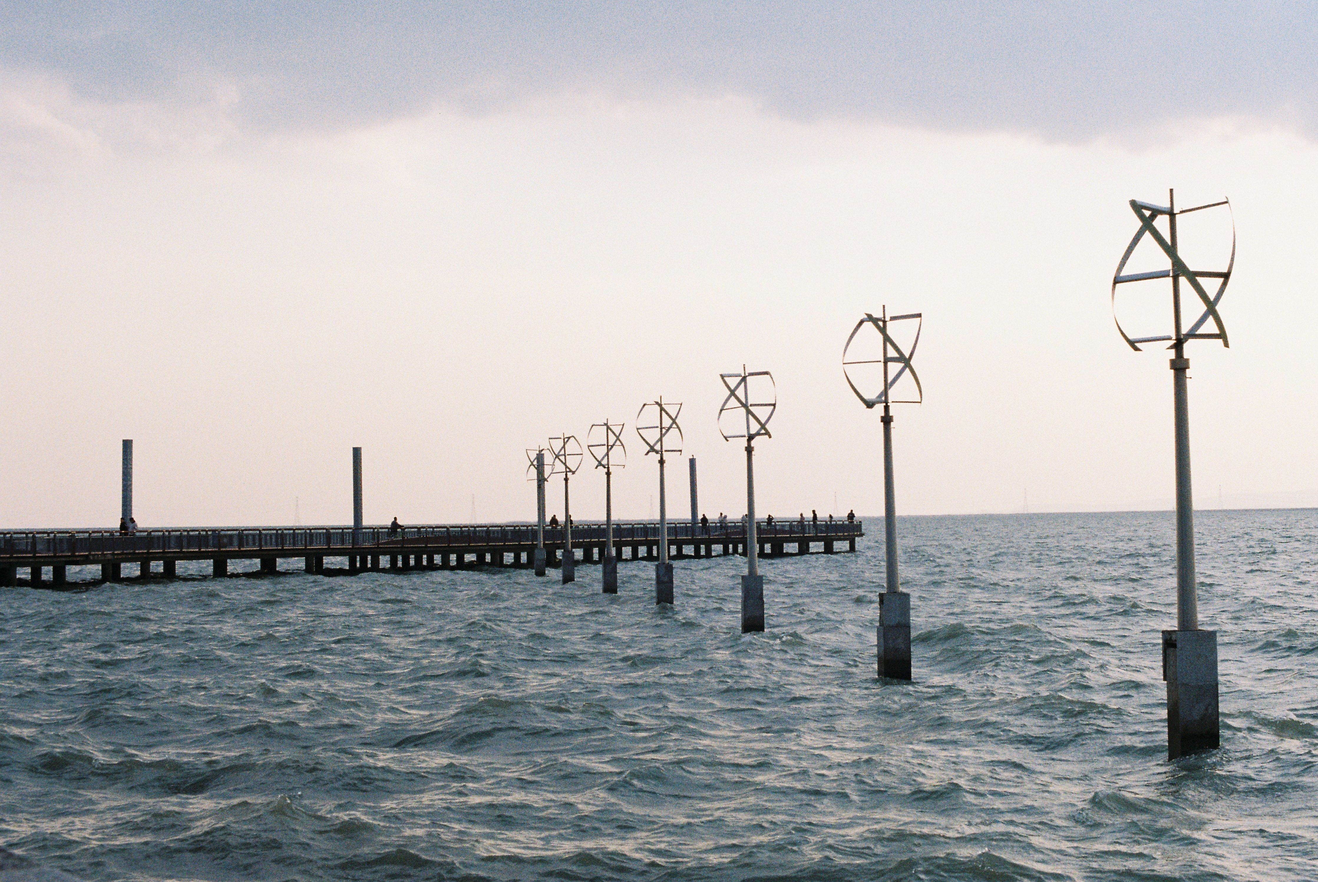 Series of wind turbines by a pier over the sea at dawn, symbolizing renewable energy.