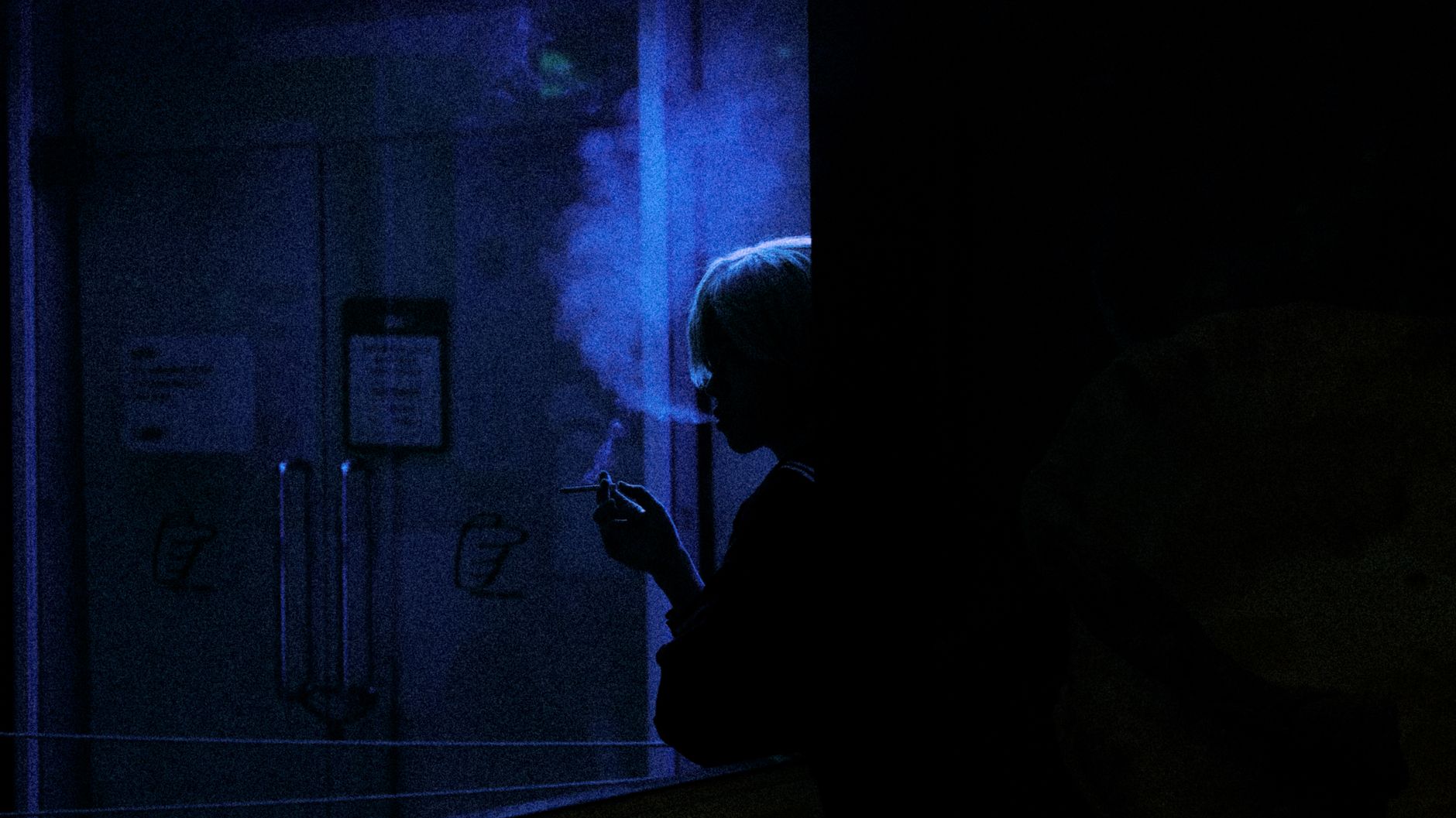 Silhouette of a person smoking indoors with blue ambient light and smoke.