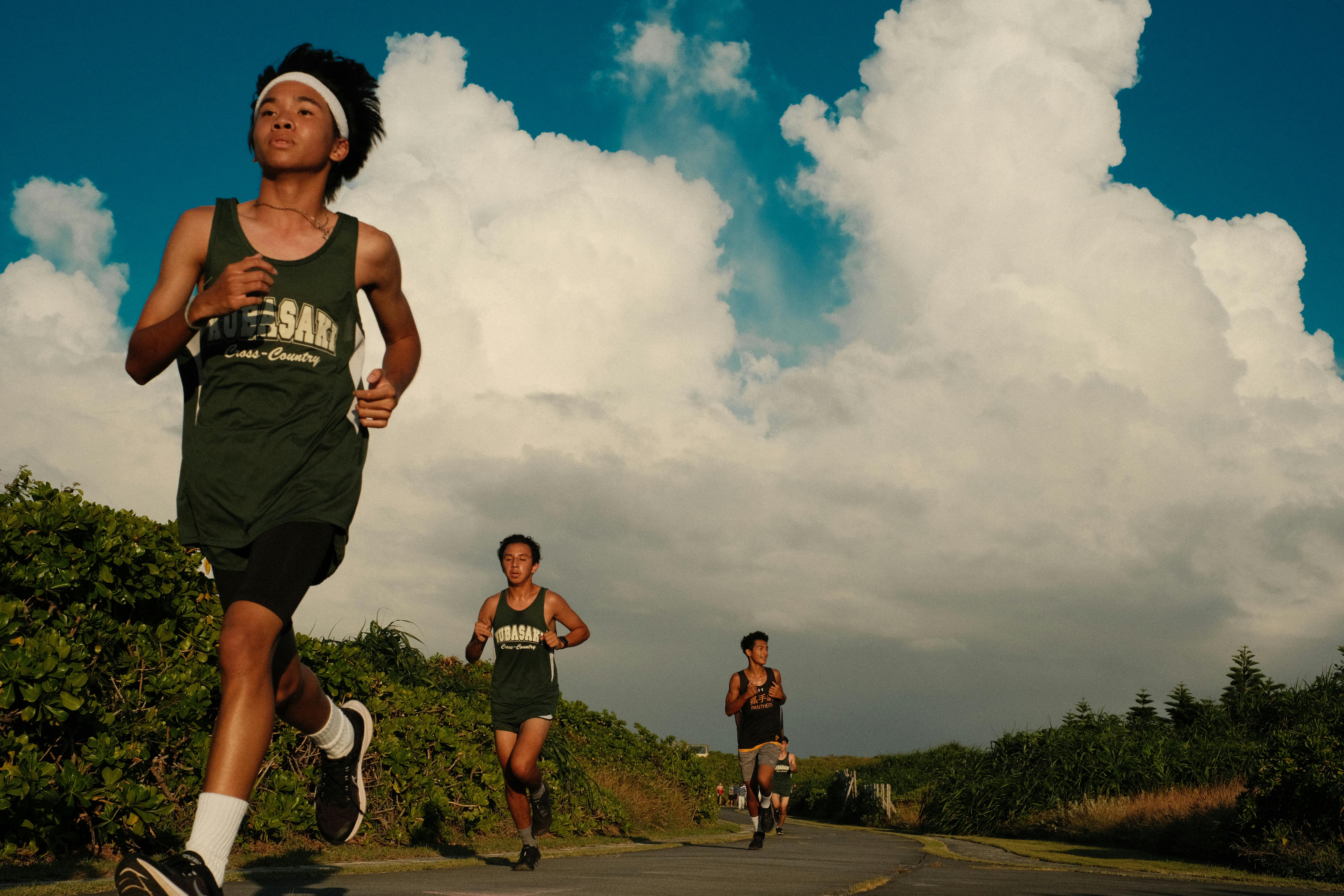 Three teenage boys jogging on a sunny day with dramatic clouds in the background. Perfect for fitness and lifestyle themes.