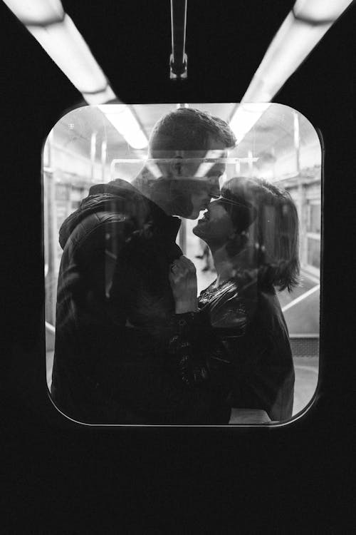 電車の中で立っている間に女性の鼻にキスする男性のグレースケール写真