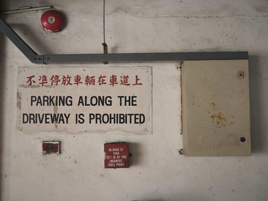Bilingual parking prohibition sign on an industrial indoor wall with fire safety equipment.
