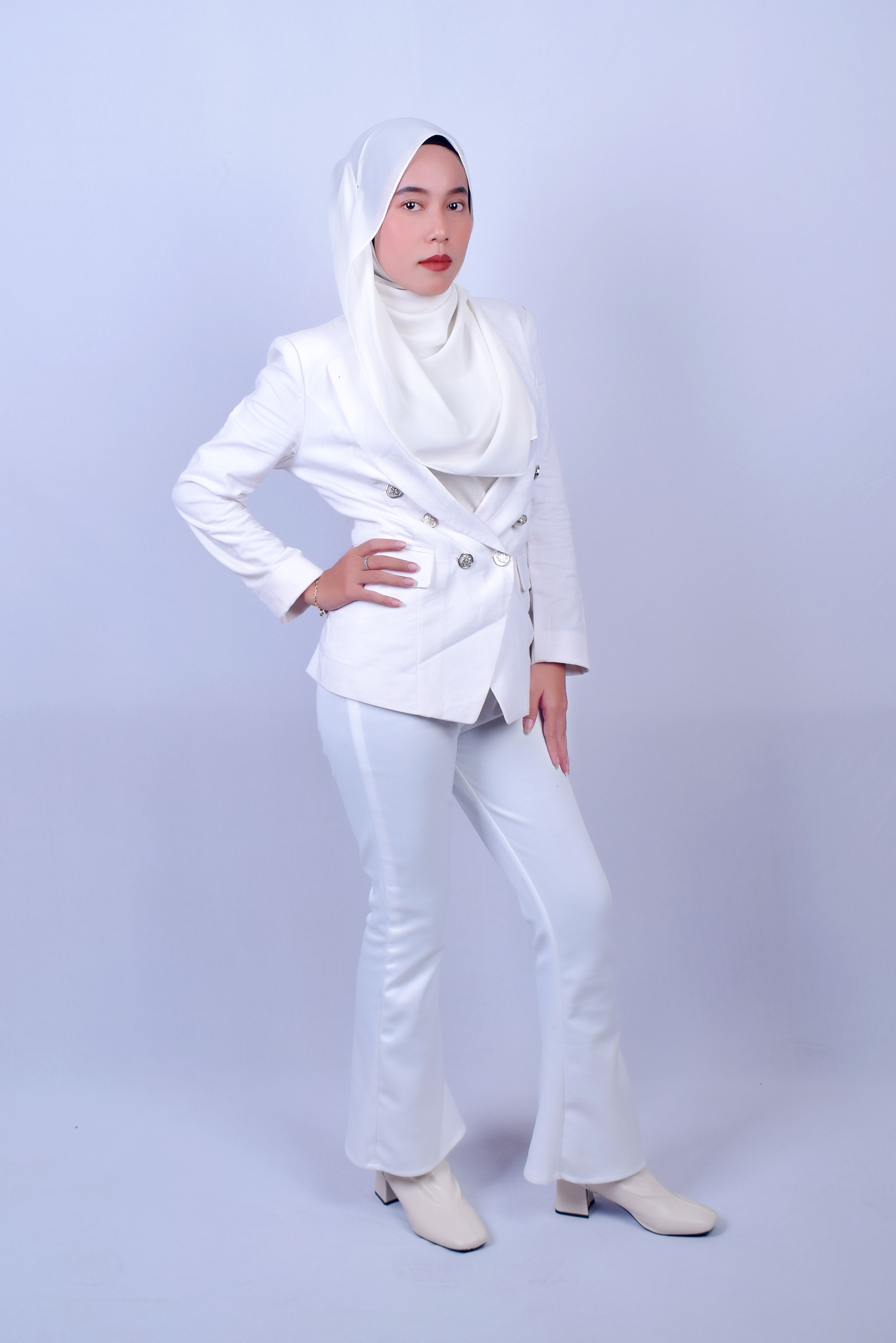 Young woman wearing white suit and hijab posing confidently in studio setting.