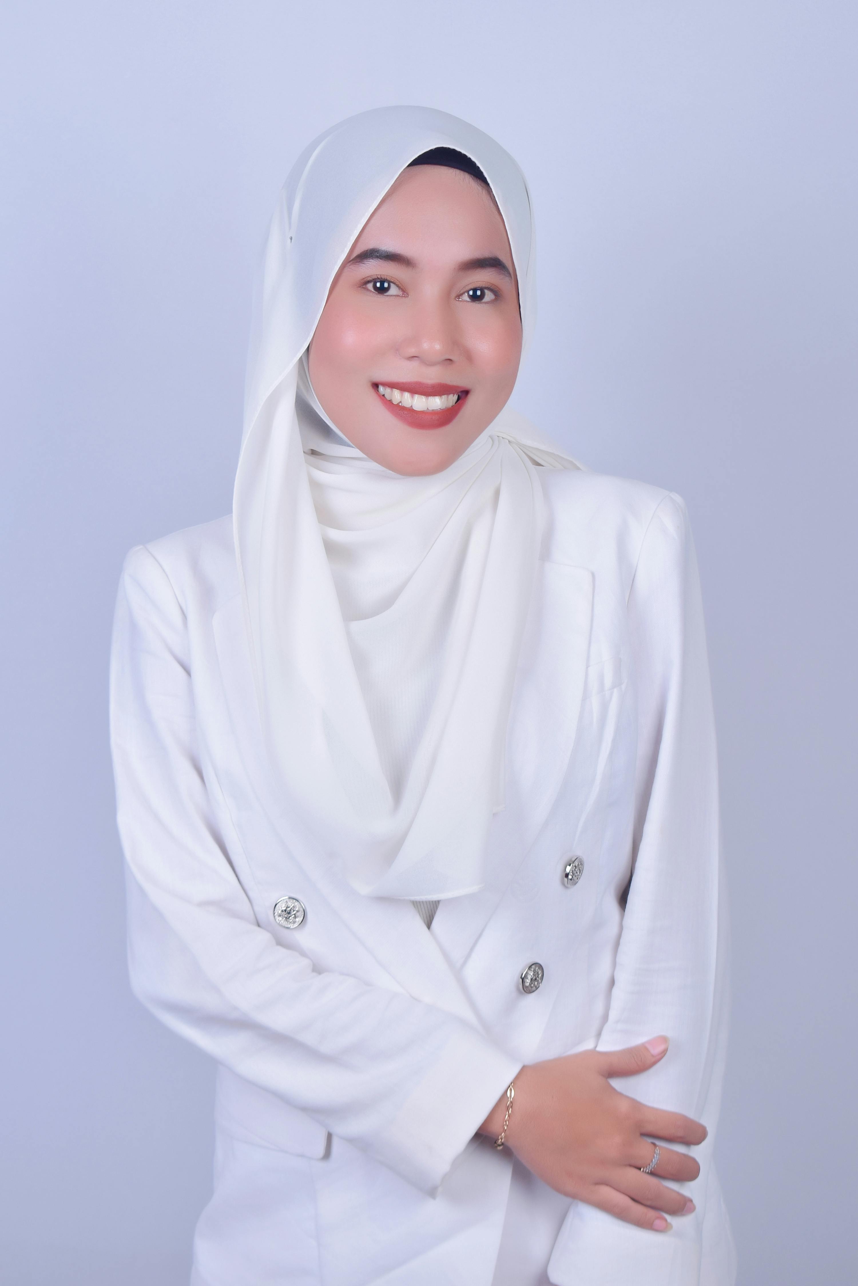 Portrait of a smiling woman wearing a white hijab and blazer against a neutral background.