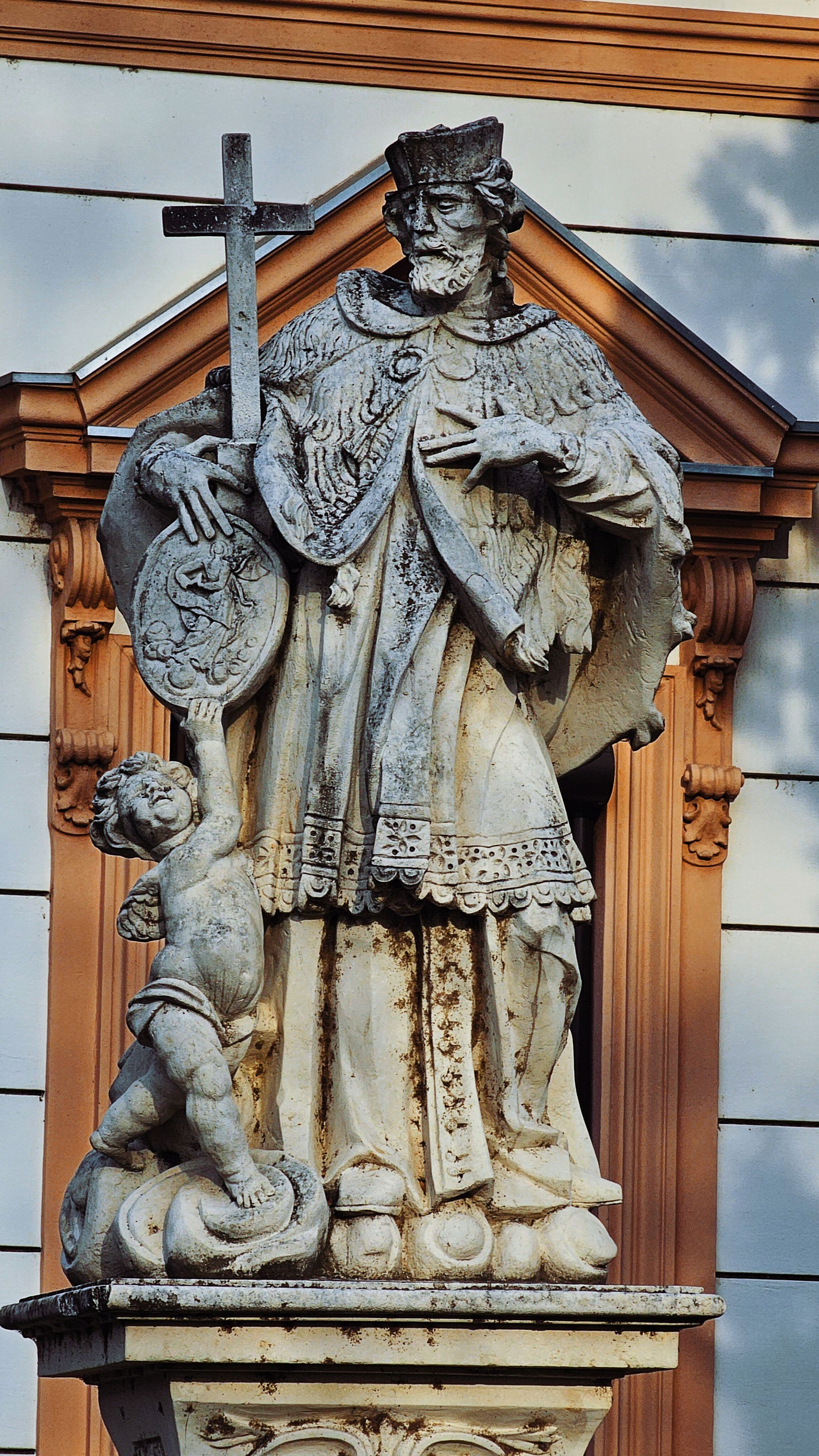 Intricately carved Baroque statue depicting a saint with a cross and cherub.