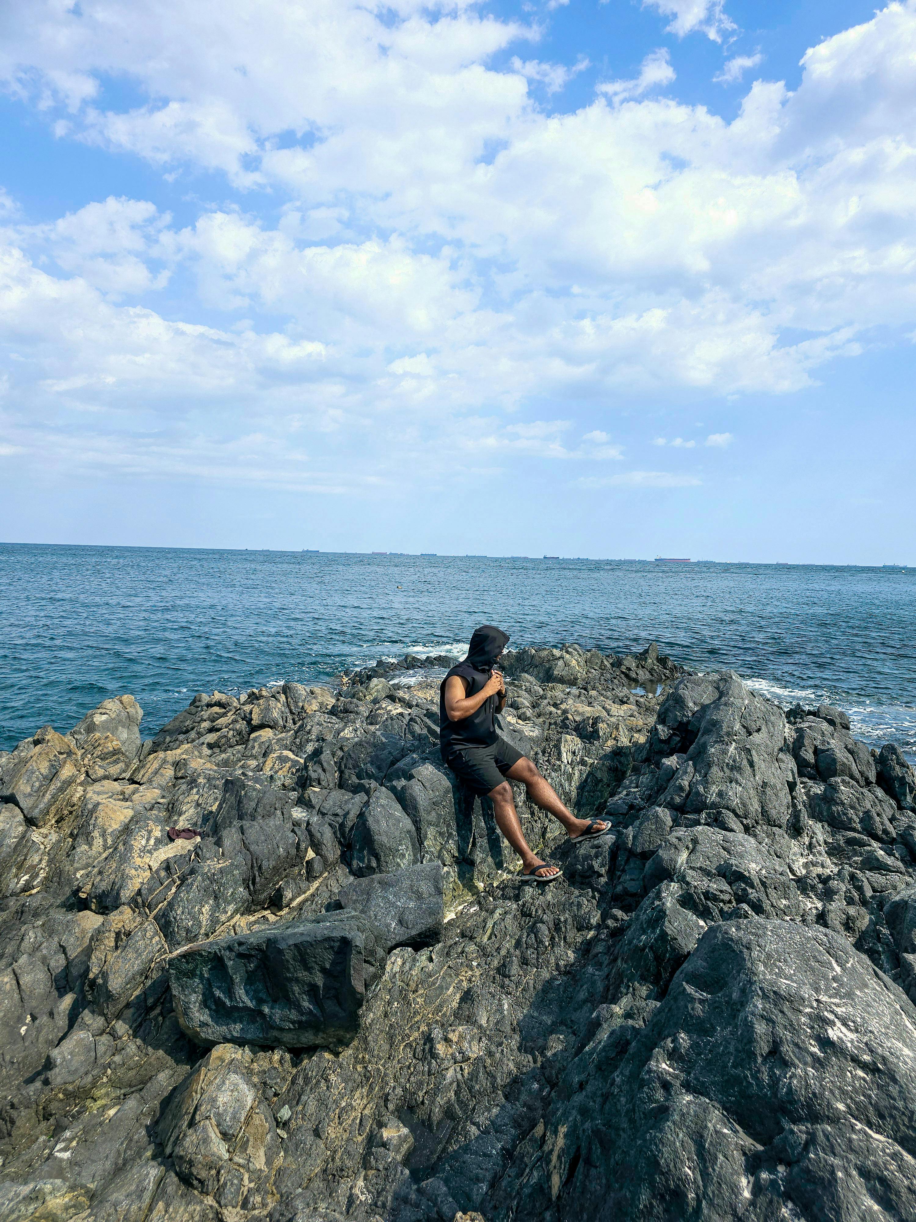 A person standing on rocky shoreline enjoying the expansive ocean view under a partly cloudy sky.