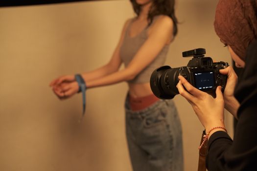 Photographer taking a close-up shot of a model with hands tied by a ribbon indoors.