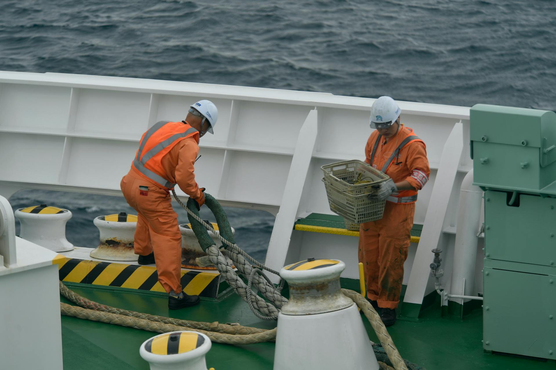 Crew members in orange uniforms working on a ship deck at sea, focusing on maritime operations.