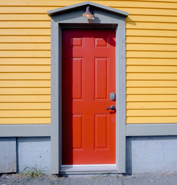 A striking red door contrasting against a yellow wooden wall, showcasing vibrant architecture.