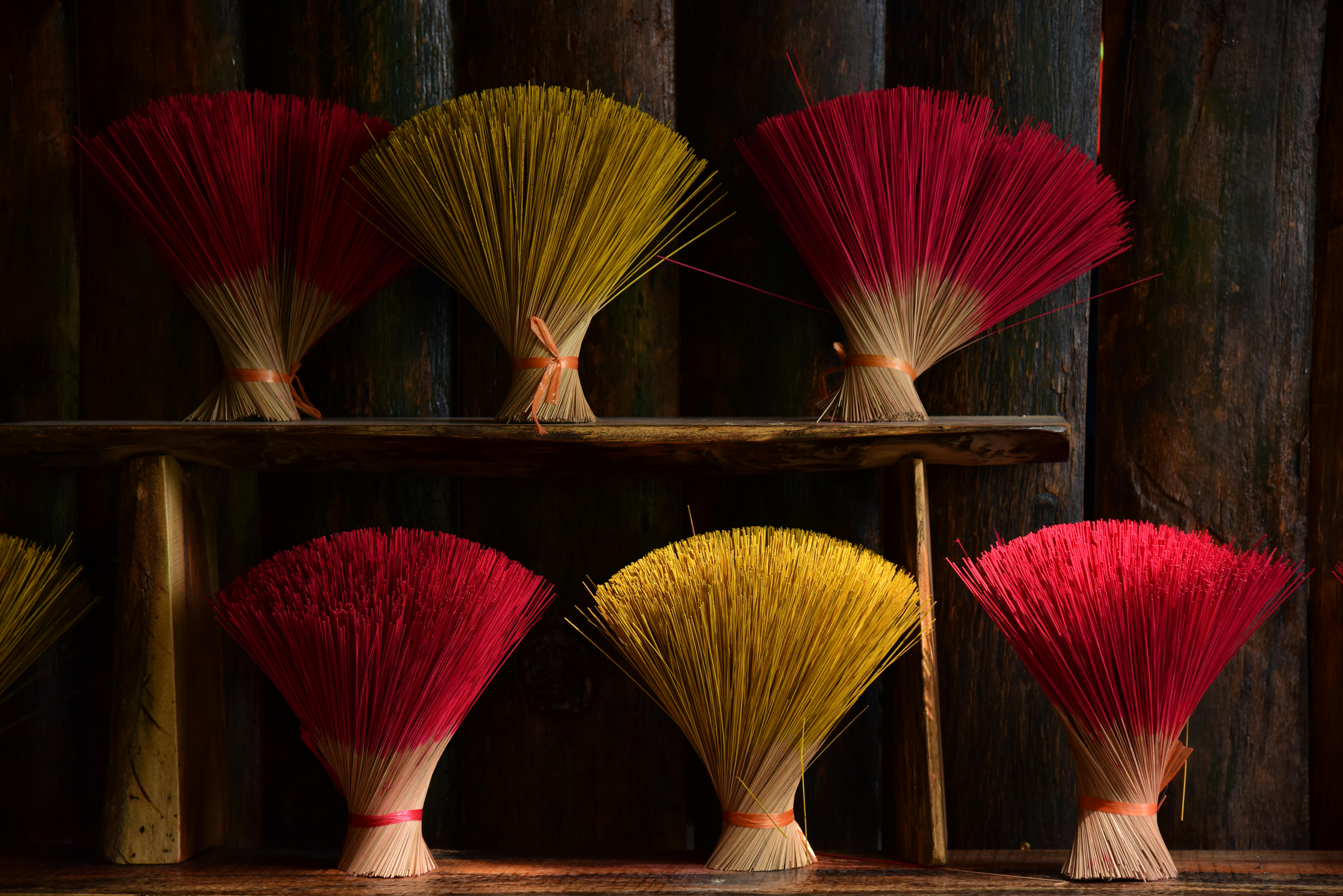 Vibrant incense stick bundles in red and yellow on a rustic wooden shelf.