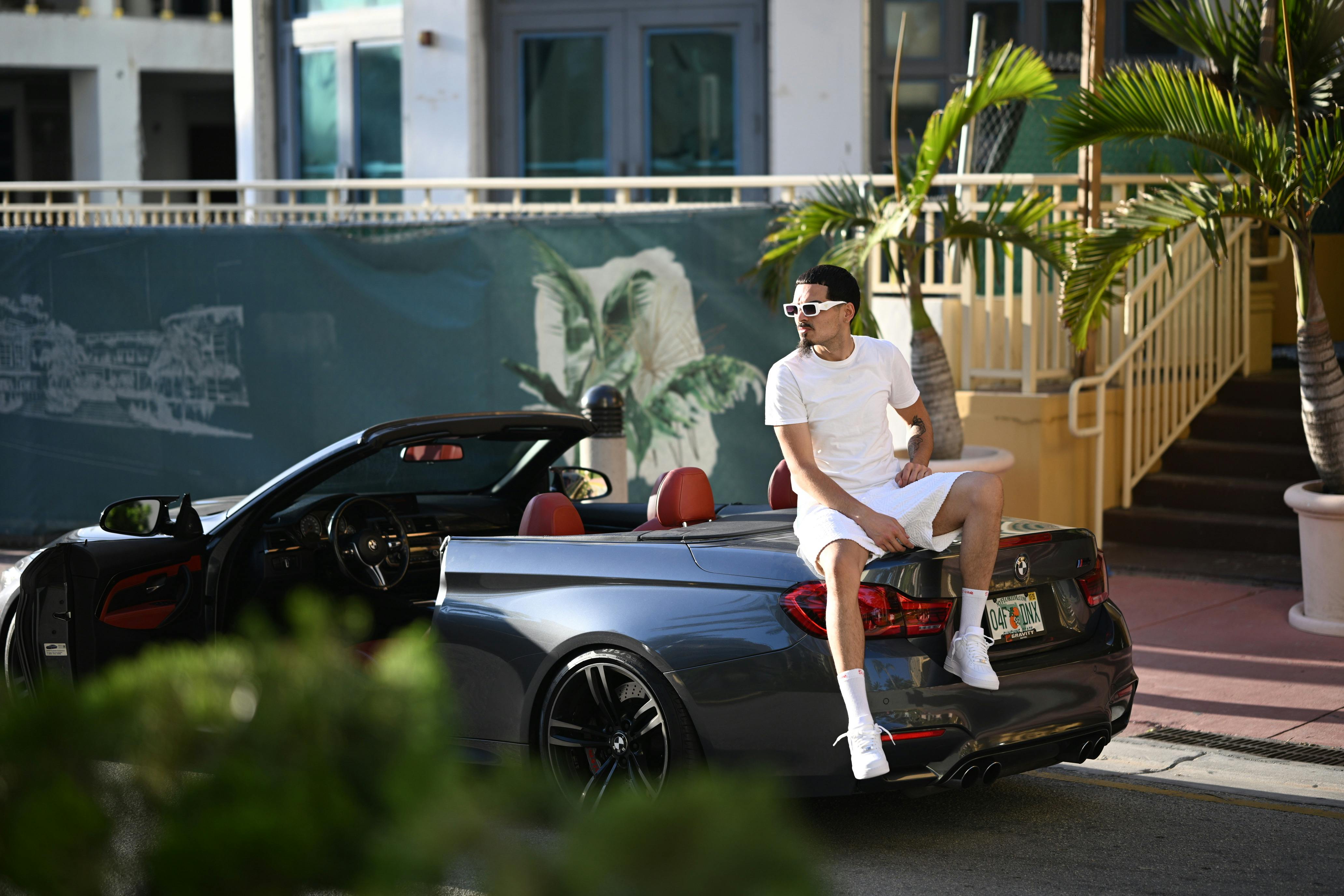 Trendy young man in white outfit sitting on a convertible car in vibrant Miami Beach.