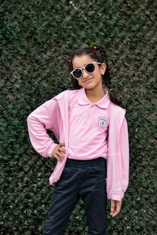 Free Girl posing confidently in casual pink outfit with sunglasses against a green background. Stock Photo