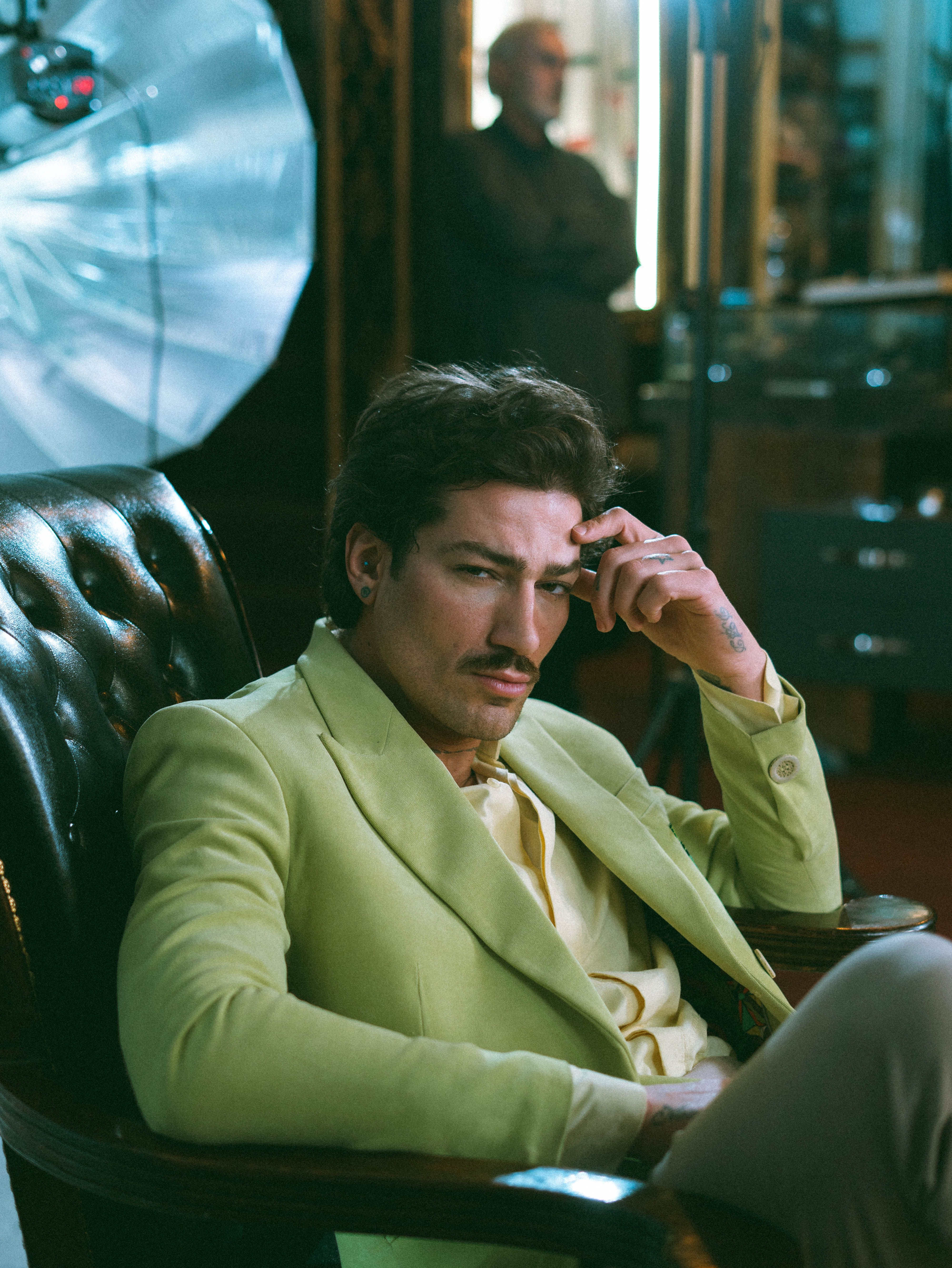 A contemplative man in a green suit sits in a vintage studio, capturing elegance.