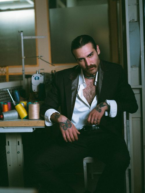 Free Tattooed man exudes confidence in a tailored suit, surrounded by sewing tools in a workshop. Stock Photo