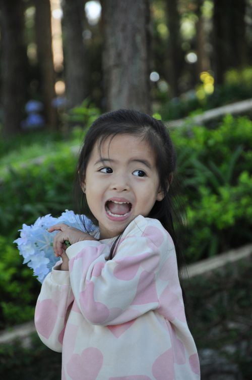Free Charming portrait of a joyful Asian child holding flowers in a lush outdoor setting. Stock Photo