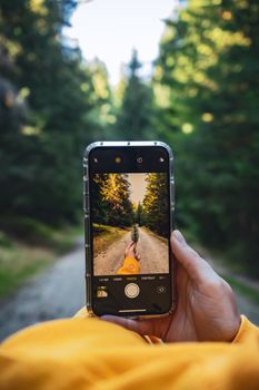 A person captures a forest path with a smartphone, showcasing autumn colors and outdoor exploration.