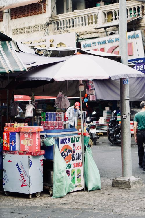 Free A vibrant street market stall with colorful drinks and large umbrella in a busy urban setting. Stock Photo