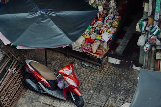 Overhead shot of a vibrant street market with a parked scooter beside a variety of goods.