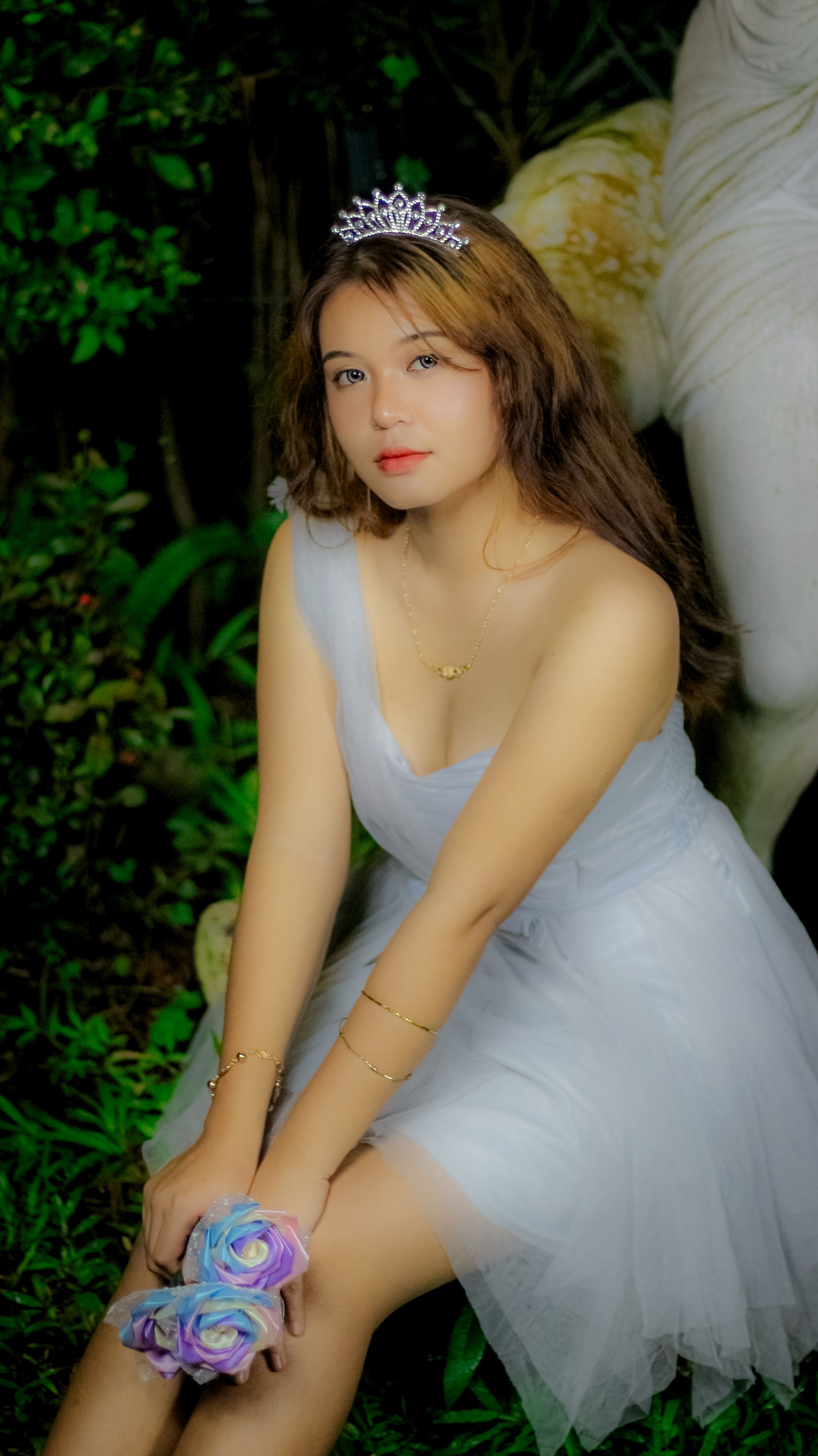 A woman in a white dress wearing a tiara, sitting gracefully with vibrant flowers.