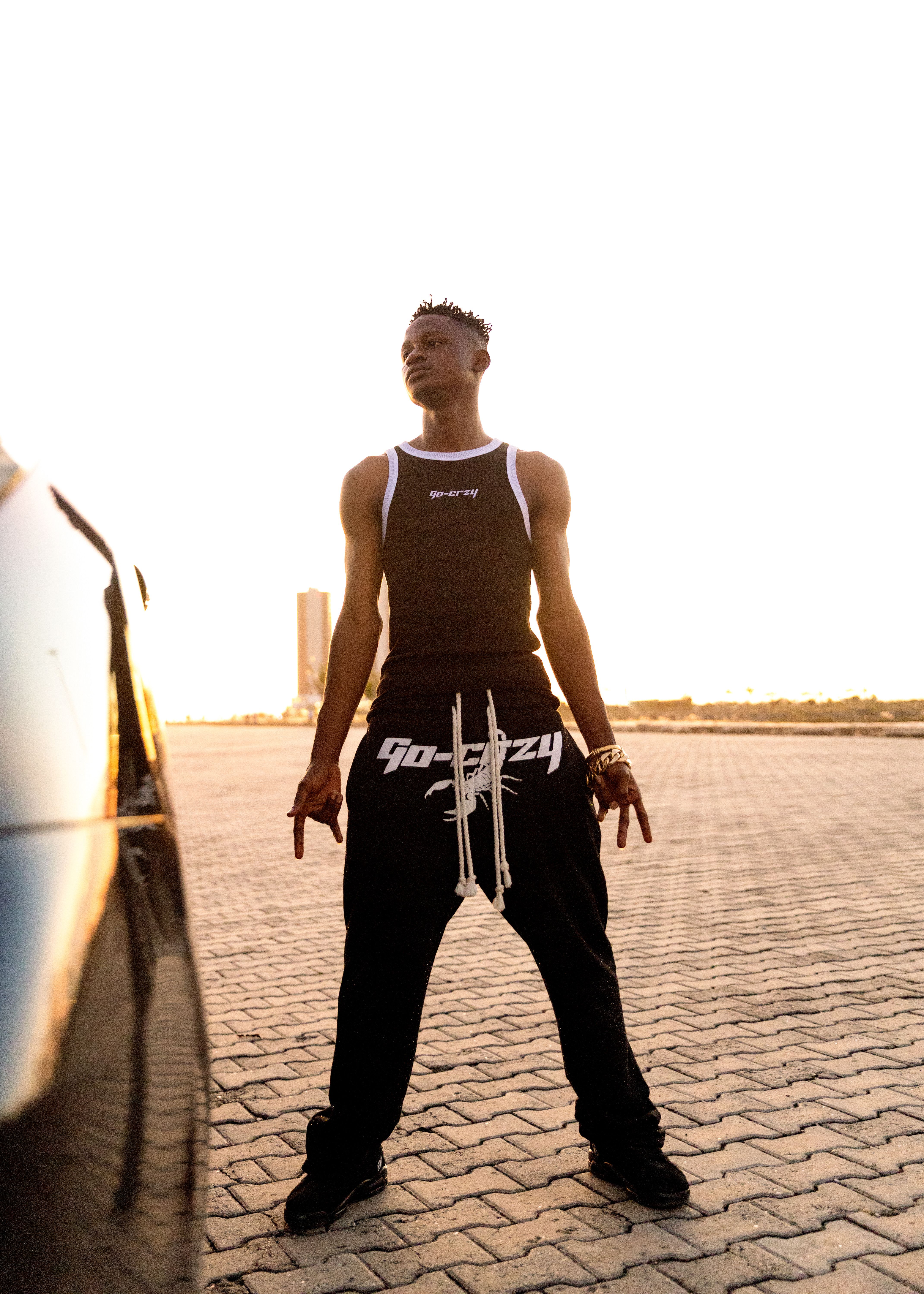 Young man in stylish attire posing on a paved street with sunset glow.