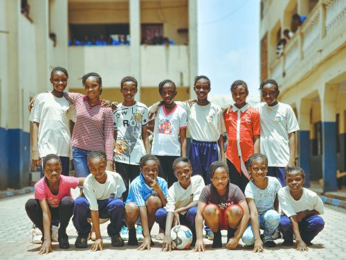 Free A group of cheerful girls posing with a soccer ball in an outdoor setting, showcasing team spirit. Stock Photo