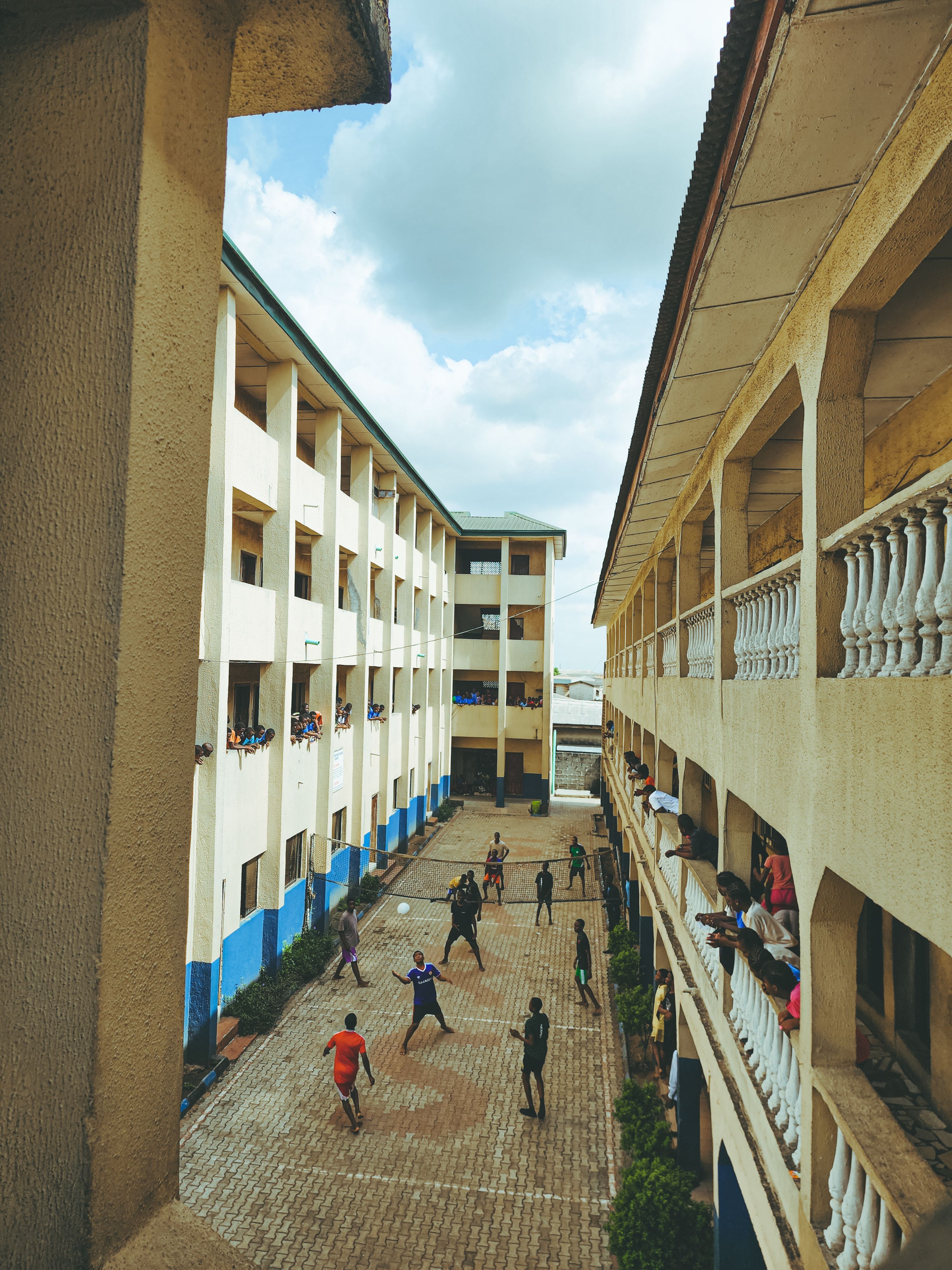 A busy school courtyard with students playing a game of volleyball between buildings.