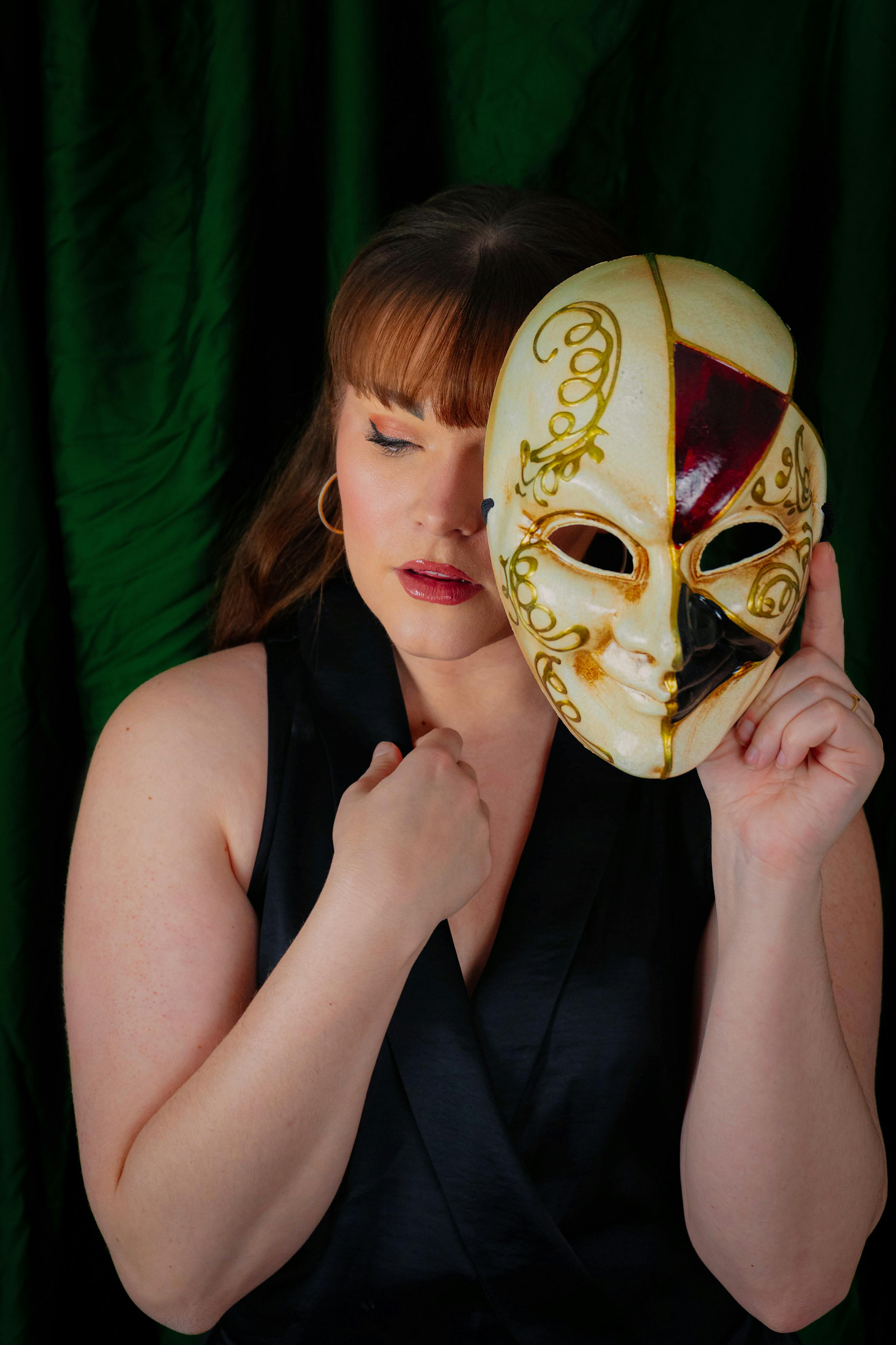 Free A woman holding a decorative masquerade mask showcases elegance and mystery in a dramatic portrait. Stock Photo