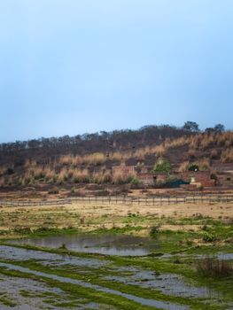 A serene view of the rural countryside featuring hills, fields, and a small water body under a cloudy sky.