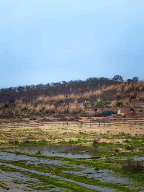 Free A serene view of the rural countryside featuring hills, fields, and a small water body under a cloudy sky. Stock Photo